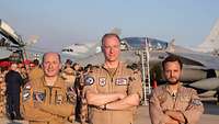 Three pilots stand in front of fighter jets