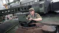 Ein Soldat schaut aus der Luke eines Panzers, vor ihm liegt ein aufgeklappter Laptop.