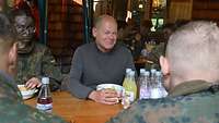 Olaf Scholz sitzt lächelnd mit Soldaten an einem langen Tisch, auf dem Getränkeflaschen stehen.