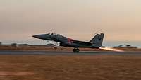 A fighter jet takes off from an airfield at dawn.