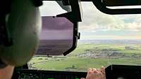 Ein Pilot schaut aus der Frontscheibe eines Flugzeugs während des Flugs auf eine grüne Landschaft.