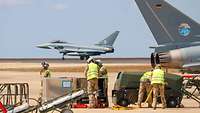 A Eurofighter rolls over the airfield while work is being carried out in the foreground.