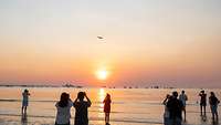 As the sun sets over the sea, a jet flies over the water