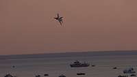  A jet flies in the last sunlight over the ships anchored for the air show