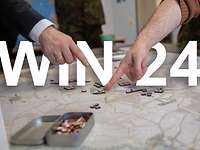 A wargame map is lying on the table. In front of the ‘Win 24’ lettering, two fingers are pointing towards playing pieces.