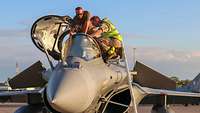 Two soldiers lean over the open cockpit of a fighter jet.