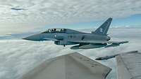 From the window of a fighter jet you can see another fighter jet flying above the clouds.