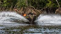 Soldaten fahren auf einem Fluss mit einem Boot, im Hintergrund sind Mangroven zu sehen