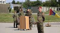 Mehrere Soldatinnen und Soldaten auf einem Appellplatz. Eine Soldatin steht hinter einem Rednerpult.