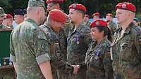 Mehrere Soldaten stehen in Formation, davor ein weiterer Soldat, der die Hand einer Soldat schüttelt