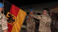 Zwei Soldaten stehen sich gegenüber und übergeben sich eine deutsche Flagge