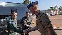 Two military men greet each other in front of a stationary car.