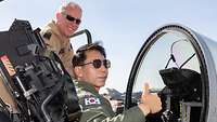 A Korean pilot sits in an open cockpit while a German pilot stands next to it.