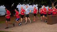 A group of runners in mostly red T-shirts in front of the waterfront.