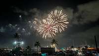 Ein Feuerwerk in der Nacht explodiert über einen Hafen, in dem Schiffe liegen