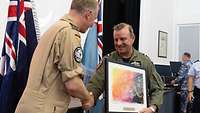 Two soldiers in flight suits shake hands and hand over a picture.