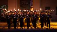 Soldaten stehen mit Fackeln in der Hand in Formation.