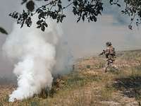 Zwei Soldaten rennen über eine Wiese. Neben ihnen steigt Rauch auf.