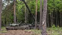 Ein Leopard-Panzer steht in einem Wald und ein Kran steht daneben