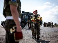 Im Vordergrund stehen zwei Soldaten hintereinander, der vordere trägt eine Flagge auf den Unterarmen