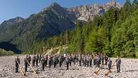 Das Gebirgsmusikkorps der Bundeswehr steht in einem ausgetrockneten Kiesbett dahinter die Alpen