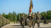 Eine Fahnenabordnung mit zahlreichen Soldaten marschiert an den angetretenen Soldaten vorbei.