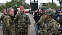 Ein Zivilist steht zwischen Soldaten vor Panzern auf einem Platz umringt von Presseleuten