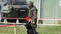 Ein Hund sitzt während der Spürhund-Ausbildung neben einem Soldaten auf einem abgesperrten Gelände.