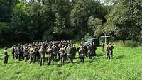 Soldaten stehen auf einer Wiese und wohnen einem Feldgottesdienst bei.