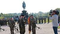 Zwei Soldaten stehen in einem Park und übergeben sich eine Flagge, die an einem Holzstab hängt