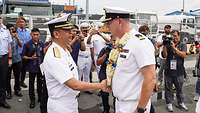 Zwei Männer in weißer Uniform schütteln sich zur Begrüßung die Hand, im Hafen von Manila.