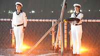 Zwei Soldaten in weißer Uniform machen an Bord eines Marineschiffes die große Flaggenparade.