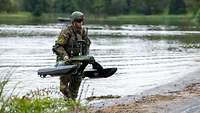 Ein Soldat, aus dem Wasser kommend, trägt ein Überwasserfahrzeug an Land.