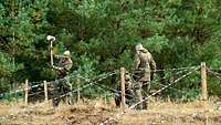 Drei Soldaten bauen einen Flandernzaun auf.