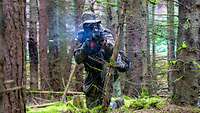 Ein Soldat kniet in einem Waldstück und schießt mit einem Gewehr G36.