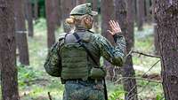 Eine Soldatin gibt im Wald Handzeichen.