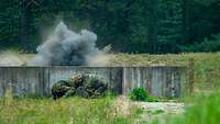 Zwei Soldaten gehen nach einem Handgranatenwurf hinter einem Betonwall in Deckung.