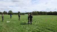 Eine Gruppe Soldatinnen und Soldaten steht auf einer Wiese und steuert Drohnen. 