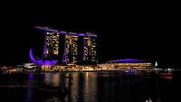 Ein beleuchtetes Hotel mit besonderer Architektur in der Marina Bay von Singapur bei Nacht.