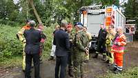 Menschen in verschiedenen Uniformen und in Zivil stehen auf einem Waldweg und sprechen miteinander.