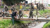 Mehrere Soldaten bauen eine Holzbrücke über einem Bachlauf