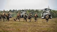 Mehrere Soldaten laufen in voller Ausrüstung über ein Feld zu mehreren Hubschraubern.