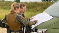 Zwei Soldaten stehen an der Motorhaube eines Fahrzeug und beugen sich über eine Skizze.