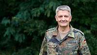 Ein General der Bundeswehr in Flecktarn steht vor einer Hecke