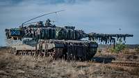 Ein Panzer dreht seinen Turm nach links und steht auf einem freien Feld