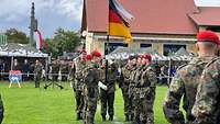 Mehrere Soldaten stehen auf einem Rasenplatz an einer Truppenfahne.