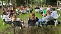 Menschen sitzen in einem Stuhlkreis auf einer Wiese