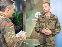 Zwei Soldaten stehen an einem Tisch vor einem Monitor während eines Interviews