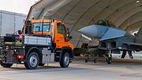 Ein Unimog schiebt einen Eurofighter rückwärts in einen Shelter