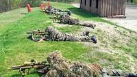 Fünf Soldaten liegen auf einer Böschung im Anschlag mit einem Gewehr.